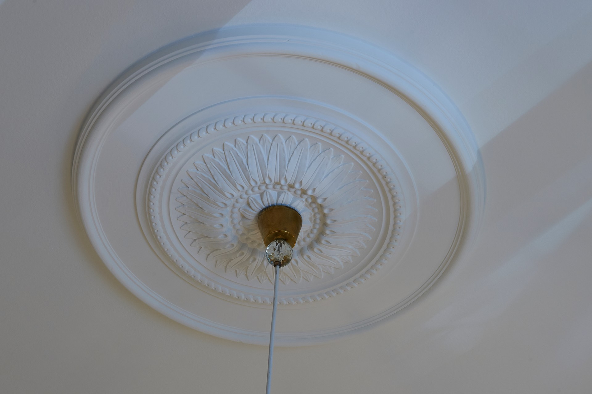 Rosetón decorativo con un intrincado relieve, que realza una lámpara colgante en un diseño de techo refinado.